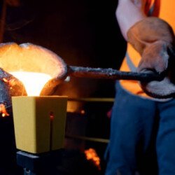 Close-up of man pouring molten steel into cast in steel mill.